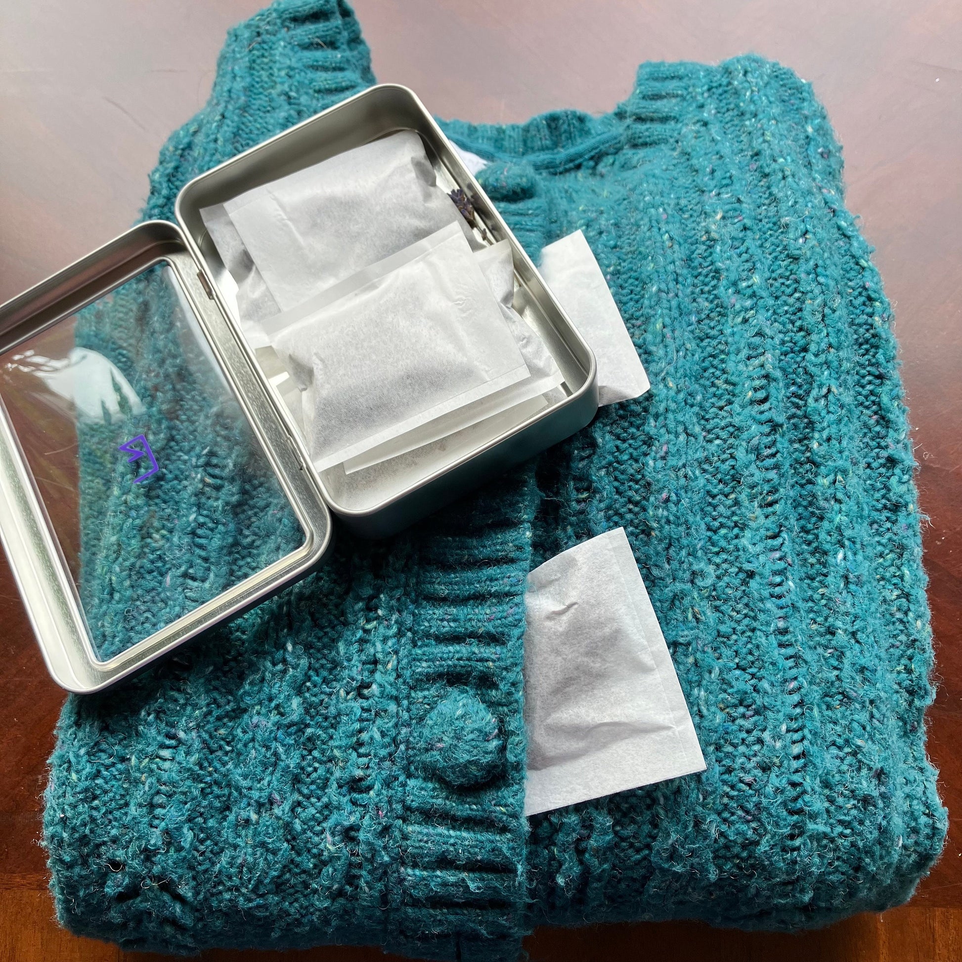 A lavender sachet resting on a folded knitted sweater, suggesting its use for freshening clothing in storage.