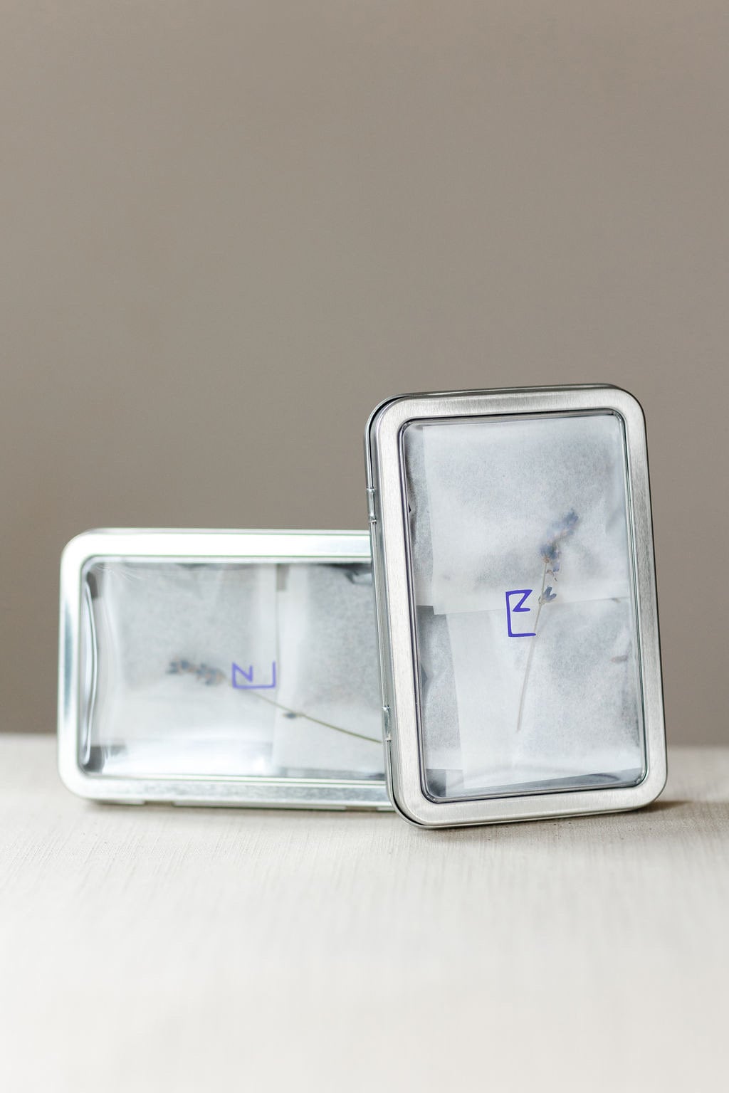 Two closed tin boxes of lavender sachets on a neutral surface, showcasing the product’s elegant and eco-friendly packaging.