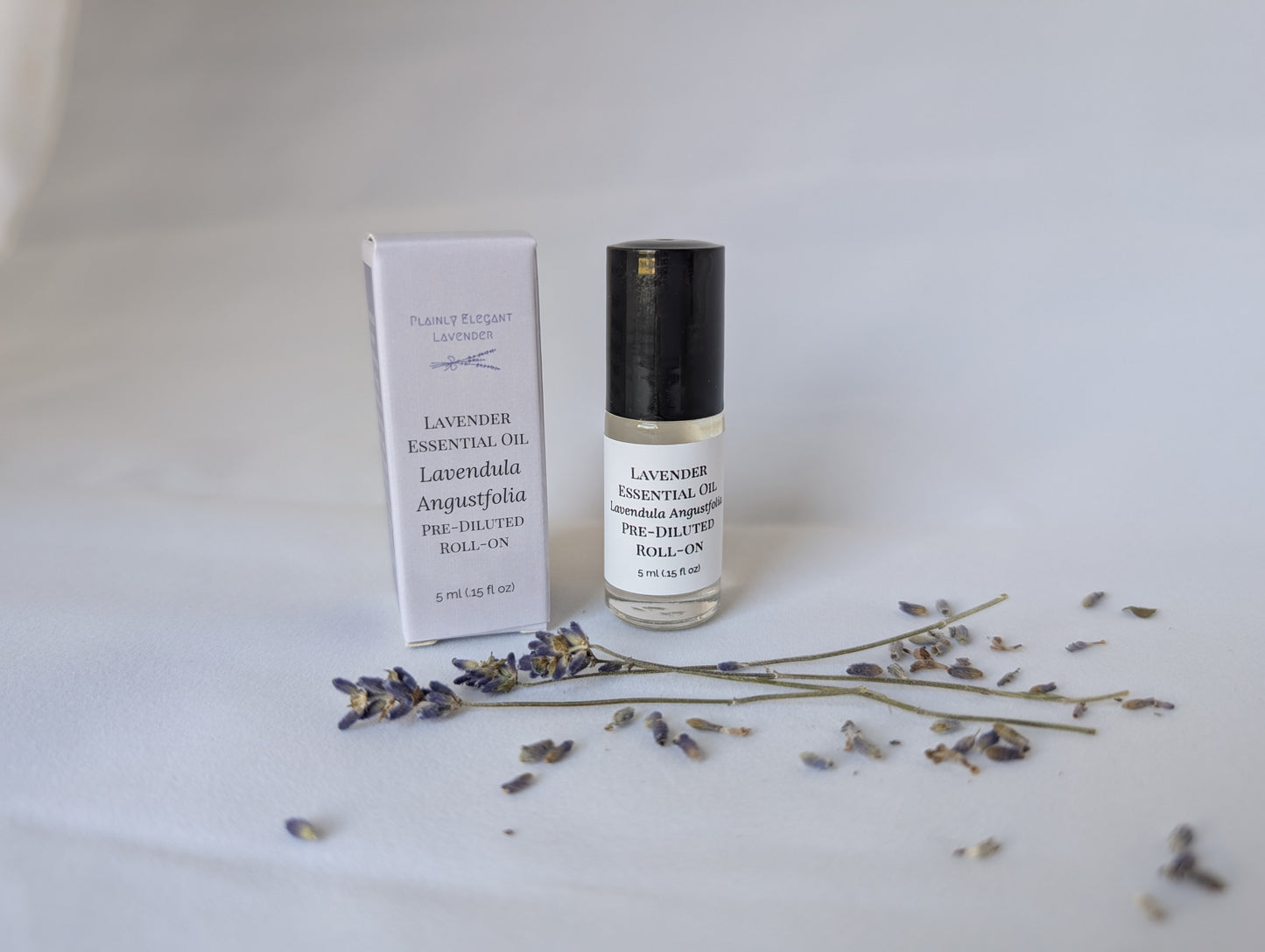 A white box and a clear roll-on bottle of Plainly Elegant Lavender essential oil, with dried lavender sprigs.