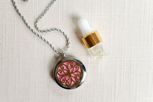 Flower locket with pink felt pad and small vial of oil on linen background