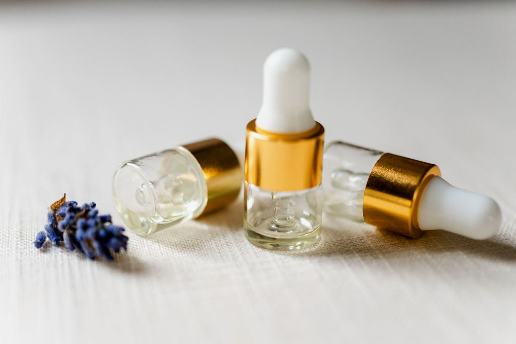 Three vials of oil with lavender buds. Each vial has a white stopper, gold rim and is clear. The oil is a good color. 