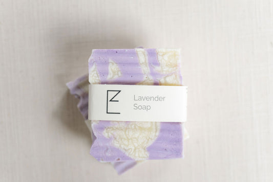 Lavender Soap. Two bars of soap stacked on top of each other on a linen background.  Both bars are a white and purple swirl.  The top shows the label : 'Lavender Soap'