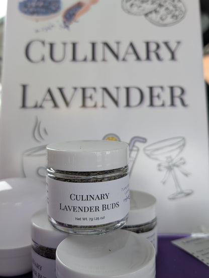 Small clear jars of Culinary Lavender Buds, 7g (.25 oz), stacked. A blurred sign in the background reads 'Culinary Lavender'.
