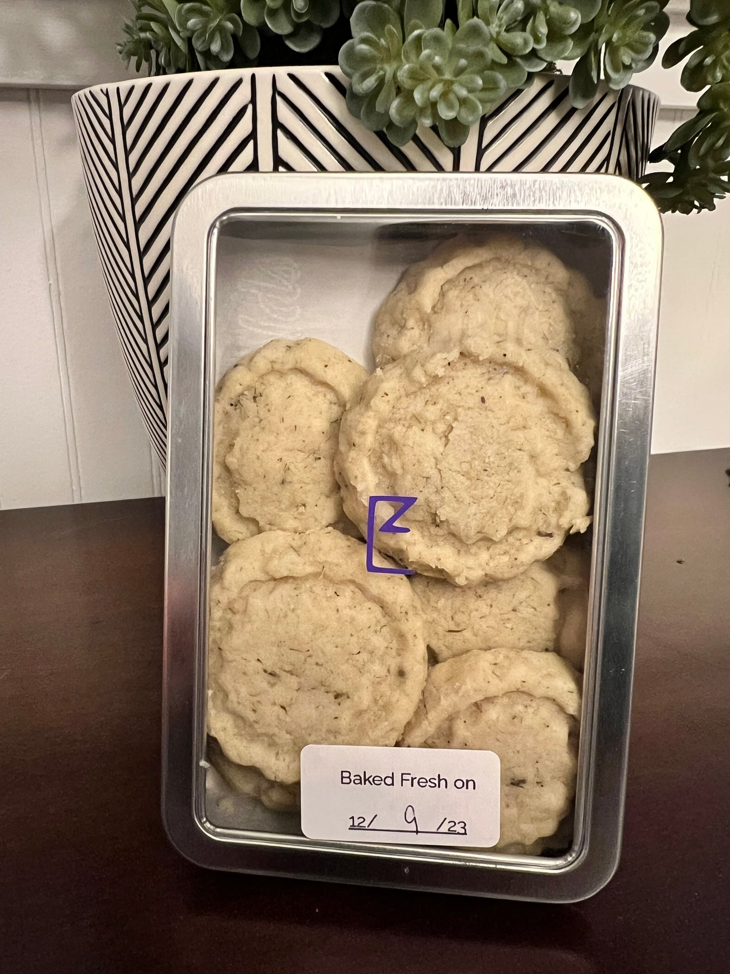 Close up of lavender shortbread cookies in a tin. Shows six round cookies, three on top, three underneath in the tin. 