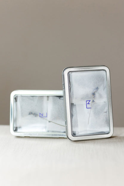 Two closed tin boxes of lavender sachets on a neutral surface, showcasing the product’s elegant and eco-friendly packaging.