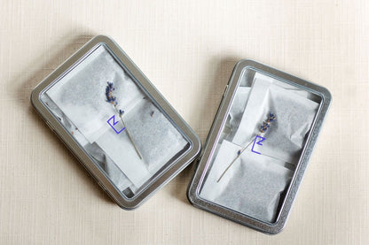 Two tin boxes of lavender sachets placed on a neutral surface, emphasizing the natural ingredients and compact size. The sachets are neatly arranged, showcasing their biodegradable packaging.